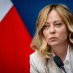 Person speaking at a conference with flag background
