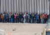 Large group of people standing near border fence
