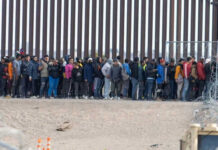 Large group of people standing near border fence