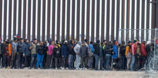 Large group of people standing near border fence