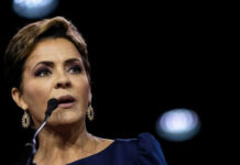 Person speaking at a microphone wearing dark clothing