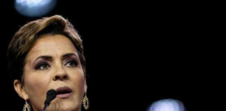 Person speaking at a microphone wearing dark clothing