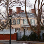 Historic mansion surrounded by bare trees and a fence