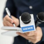 A journalist holding a notebook and microphones labeled 'NEWS'