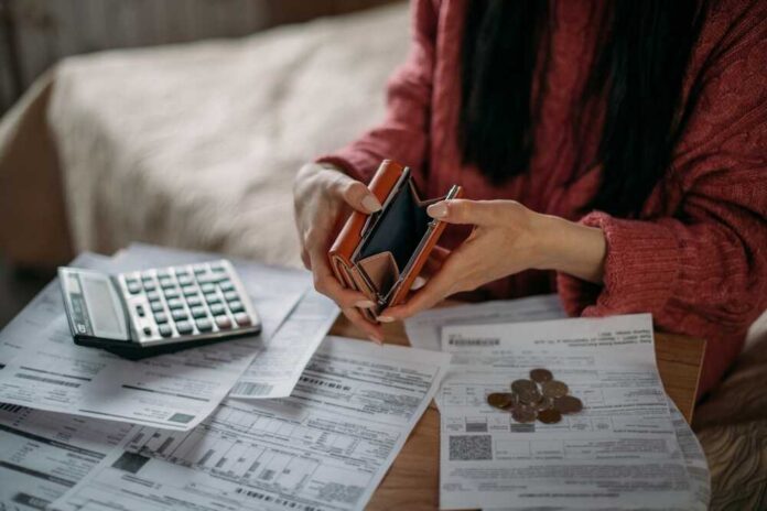 Person examining an empty wallet while surrounded by bills and a calculator