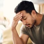 A man with a pained expression, holding his forehead in a moment of distress