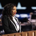 A woman in formal attire speaking at a podium with a microphone