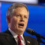 Man in formal attire speaking passionately into a microphone
