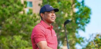 A golfer holding a club outdoors, wearing a red striped shirt