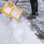 Person shoveling snow from a pathway with a yellow shovel