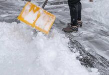 Person shoveling snow from a pathway with a yellow shovel