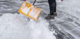 Person shoveling snow from a pathway with a yellow shovel
