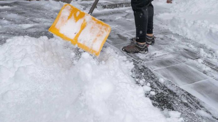 Person shoveling snow from a pathway with a yellow shovel