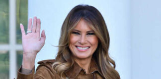 Woman waving and smiling in brown coat.
