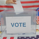 Hand placing ballot in box with American flags