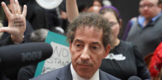A politician speaking at a protest with signs in the background