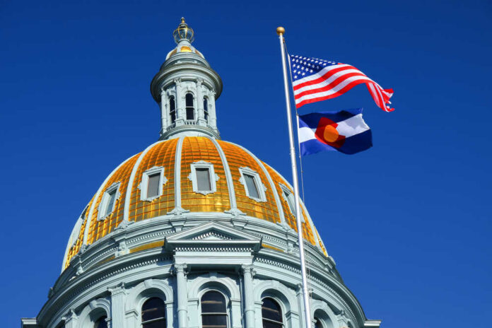The dome of a state capitol building with flags flying against a blue sky