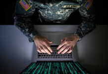 A soldier in U.S. Army uniform typing on a laptop with green code displayed on the screen