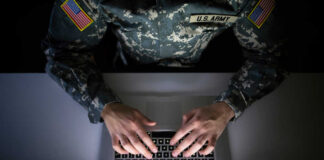 A soldier in U.S. Army uniform typing on a laptop with green code displayed on the screen
