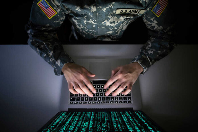 A soldier in U.S. Army uniform typing on a laptop with green code displayed on the screen