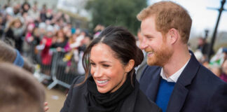 A smiling couple interacting with a crowd during a public event