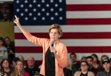 A woman speaking into a microphone with an American flag backdrop