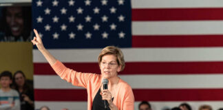 A woman speaking into a microphone with an American flag backdrop