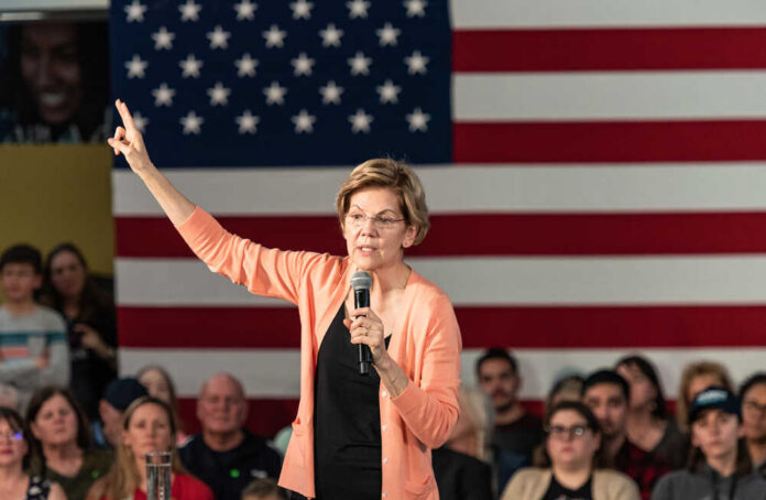 A woman speaking into a microphone with an American flag backdrop
