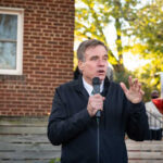 Senator’s Daughter Dies: Unity Amidst Divisive Politics A man speaking at an outdoor event with campaign signs in the background