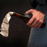 A hand holding a bottle with a cloth wick, resembling a molotov cocktail
