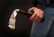 A hand holding a bottle with a cloth wick, resembling a molotov cocktail