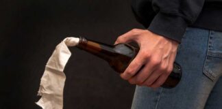 A hand holding a bottle with a cloth wick, resembling a molotov cocktail