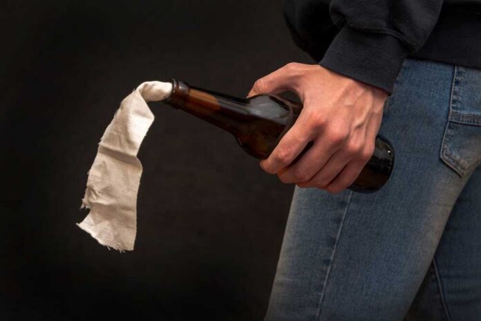 A hand holding a bottle with a cloth wick, resembling a molotov cocktail