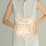 Woman in a white shirt holding her stomach with a glowing illustration of the digestive system