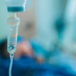 Close-up of an IV drip in a hospital setting with a patient in the background