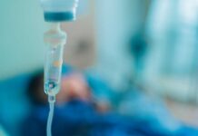 Close-up of an IV drip in a hospital setting with a patient in the background