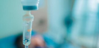 Close-up of an IV drip in a hospital setting with a patient in the background