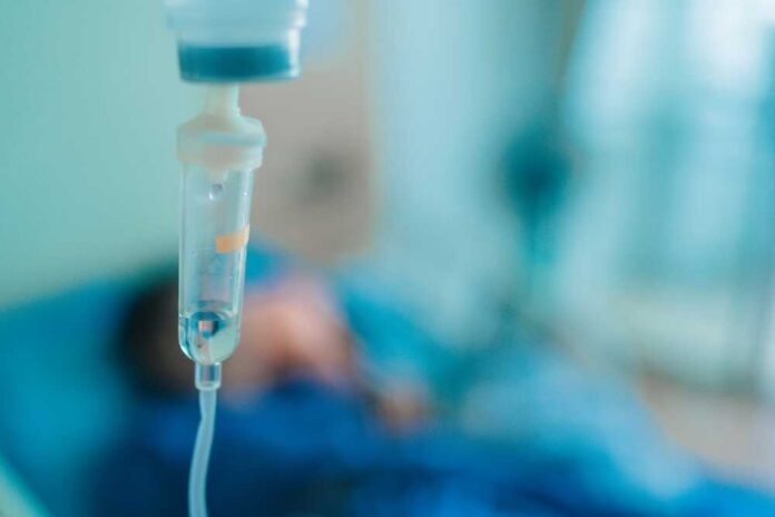 Close-up of an IV drip in a hospital setting with a patient in the background