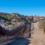 A border wall with barbed wire in a rural landscape