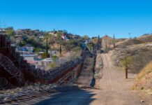 A border wall with barbed wire in a rural landscape