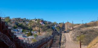 A border wall with barbed wire in a rural landscape
