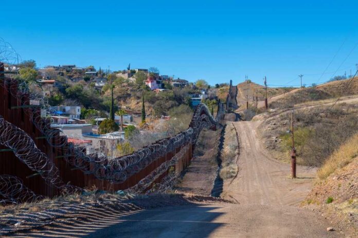 A border wall with barbed wire in a rural landscape