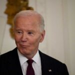 A man in a pinstripe suit smiling in an indoor setting