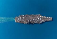 Aerial view of an aircraft carrier with fighter jets on deck in a blue ocean