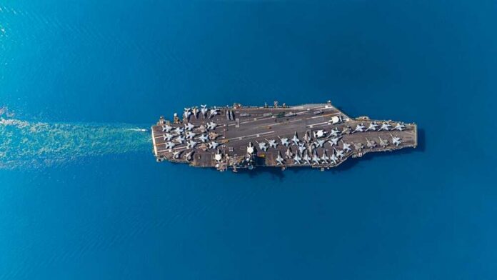 Aerial view of an aircraft carrier with fighter jets on deck in a blue ocean