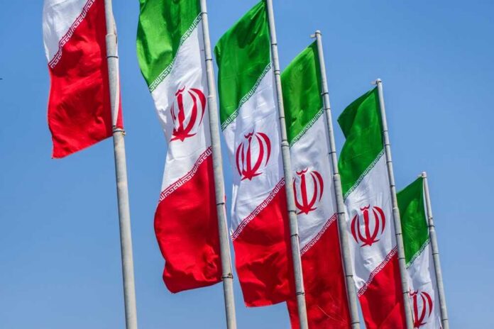 shutterstock_2610392641.jpg Multiple Iranian flags waving against a clear blue sky