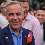 A smiling man in a blue suit surrounded by a diverse crowd at an outdoor event