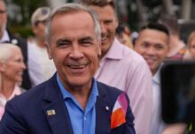 A smiling man in a blue suit surrounded by a diverse crowd at an outdoor event