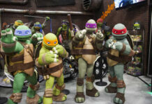 Four characters in turtle costumes posing at a convention