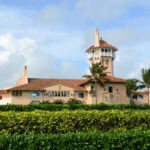 A large historic mansion with a tower surrounded by palm trees and greenery